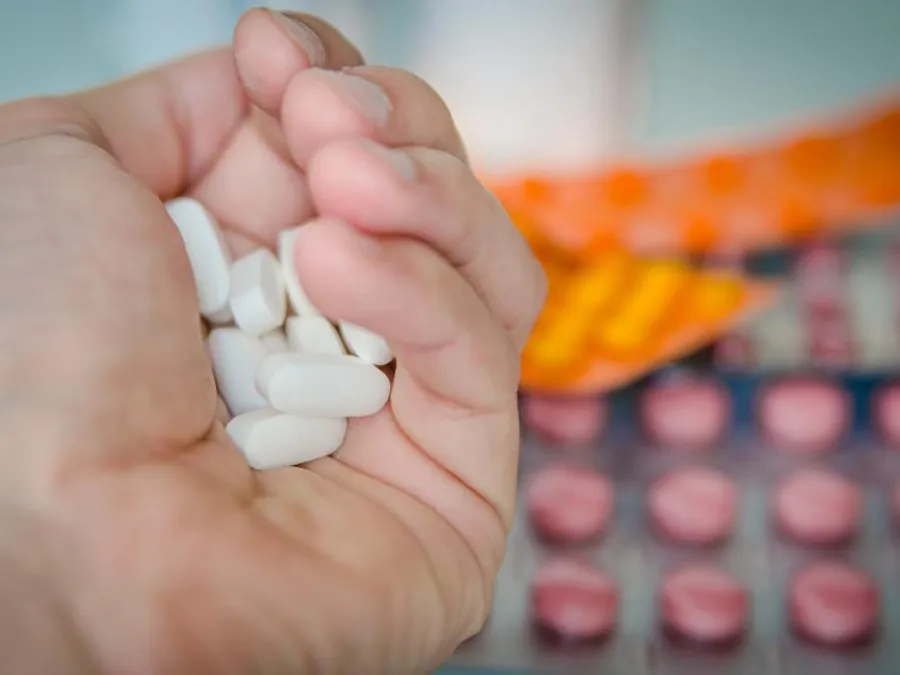 A hand holding tablets above packets of medication